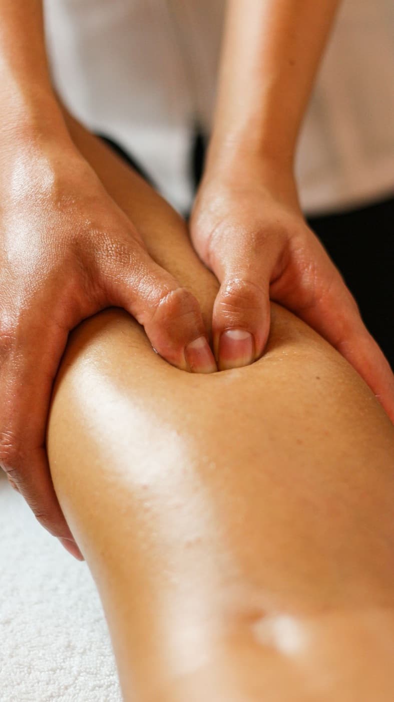 Een fysiotherapeut masseert met beide handen de kuit van een patiënt