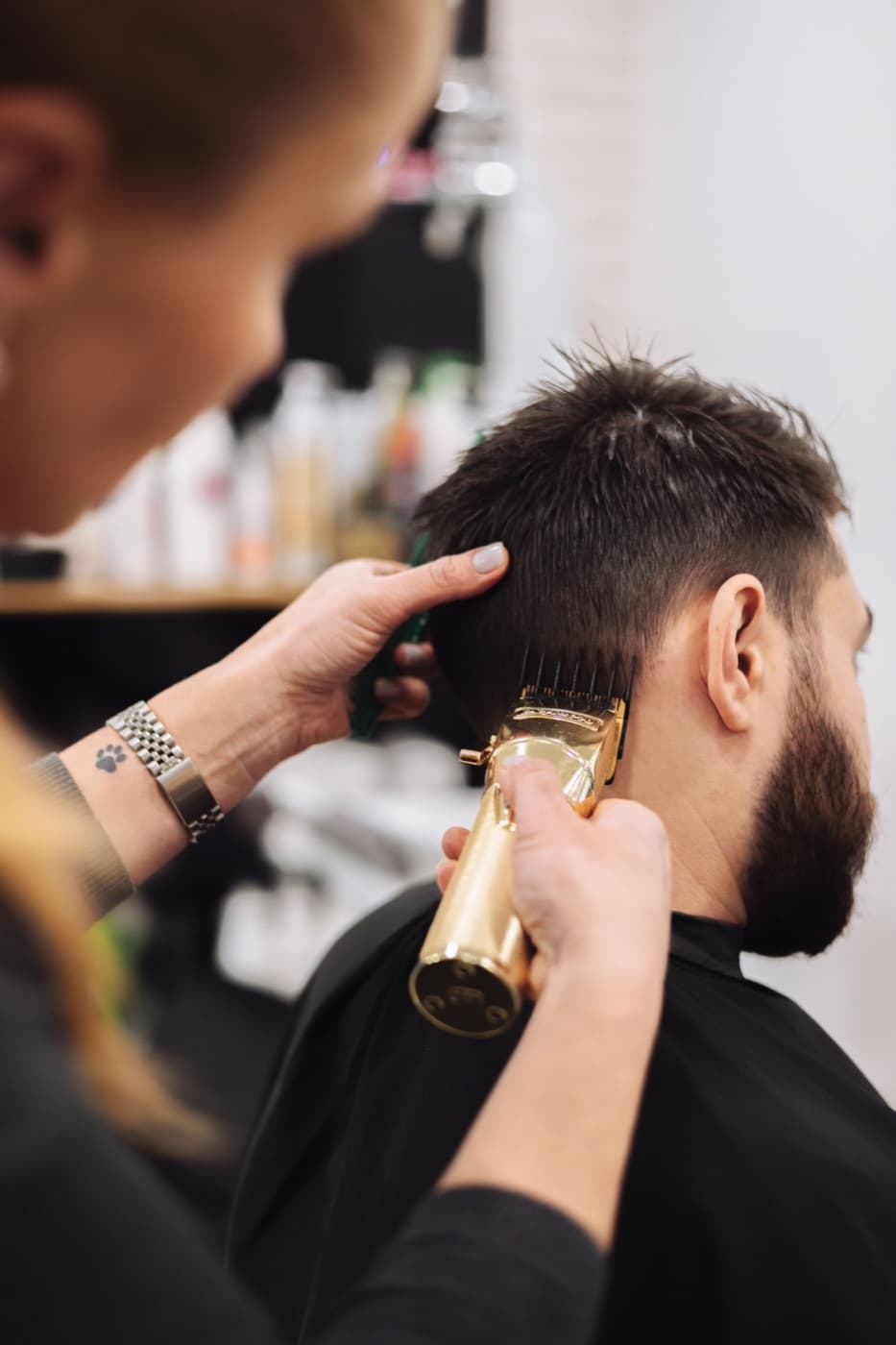 Een kapper knipt met een tondeuse het haar van een klant met baard
