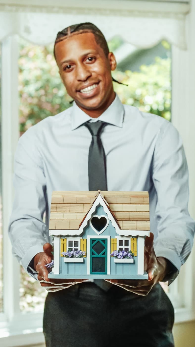 Een lachende makelaar in overhemd en stropdas houdt een maquette van een huis vast