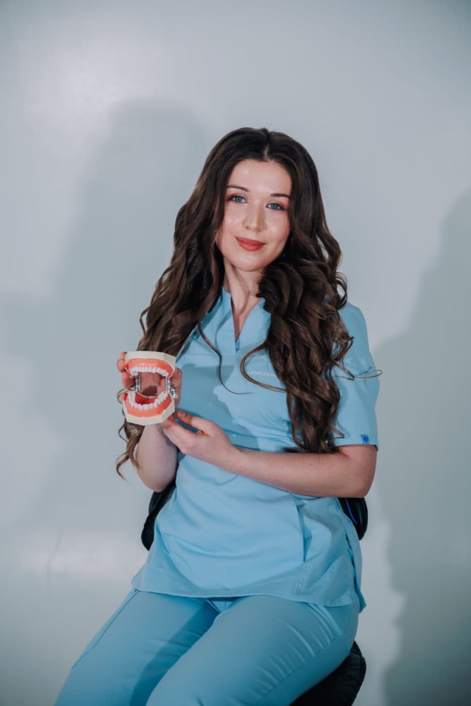 Een tandarts in een blauw uniform houdt glimlachend een gebitsmodel vast